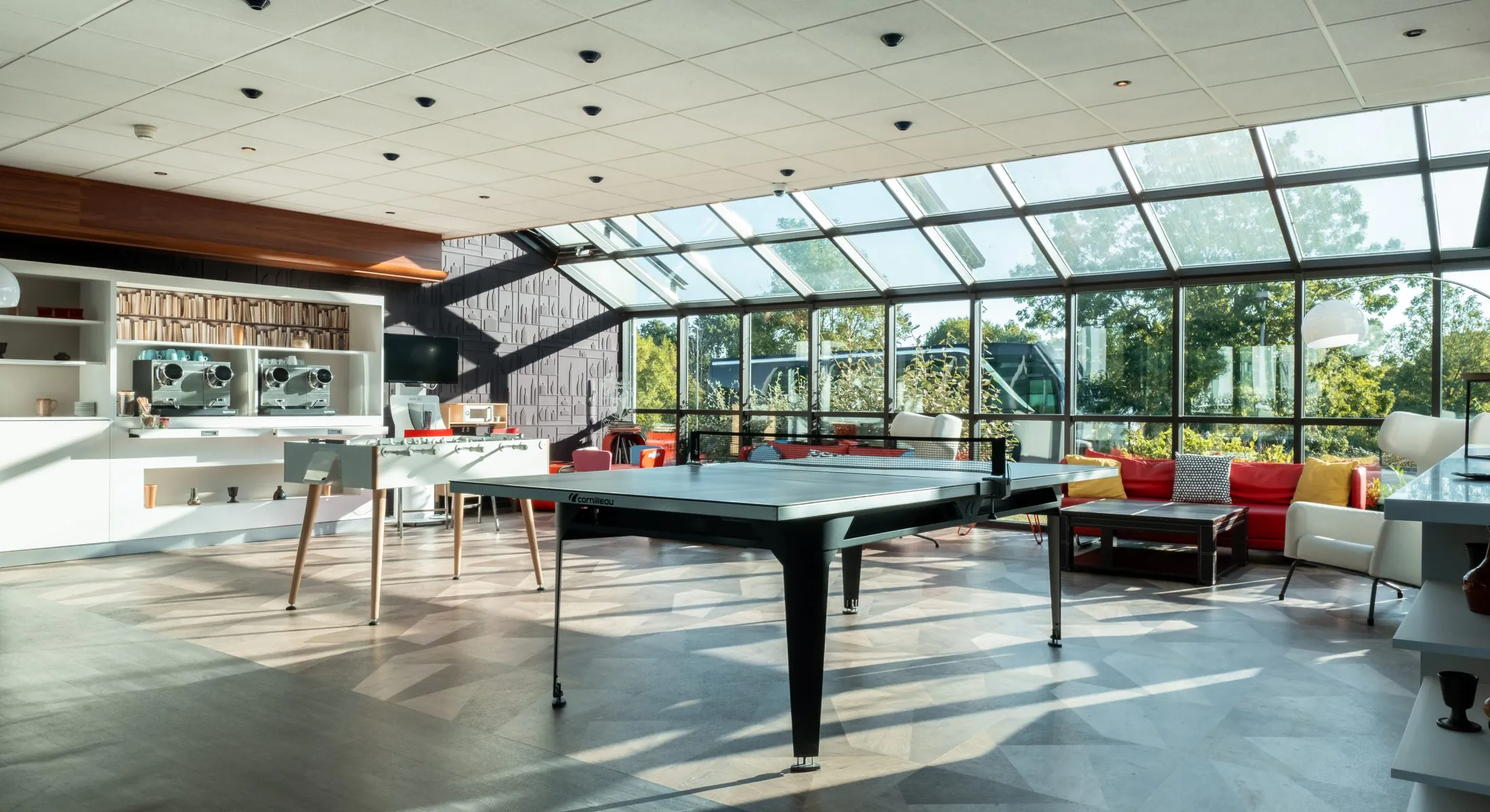 en::Glass-roofed space with a ping-pong table, table football, sofas, children’s play armchairs and a dedicated seminar break counter. fr::Espace sous verrière avec table de ping-pong, baby-foot, canapés, fauteuils de jeux pour enfants et meuble dédié aux pauses séminaires du Novotel Chartres.