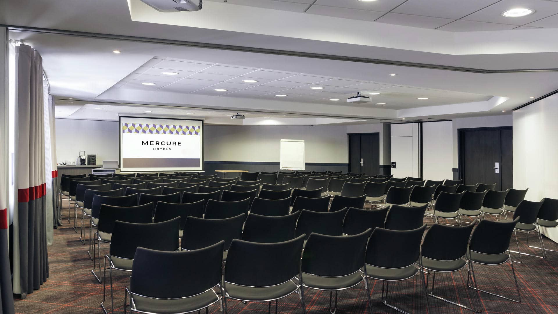rows of black chairs in front of a mercure projector screen