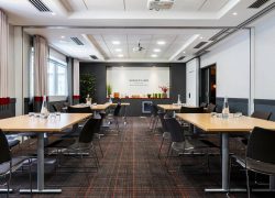 en::Bright, spotless meeting room with four table islands arranged on both sides of the room, projection screen at the front, seminar break below, and windows overlooking the city. fr::Salle de réunion lumineuse et impeccable avec quatre îlots de tables de part et d’autre de la pièce, écran de projection en face, pause séminaire en dessous et fenêtres avec vue sur la ville.