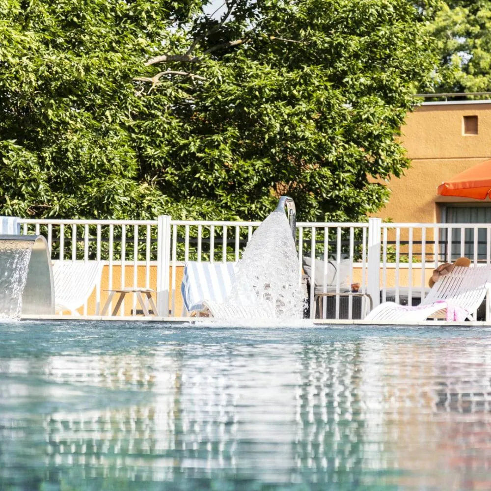 Hôtel séminaire avec piscine équipée de becs d’eau, entourée d’arbres verts.