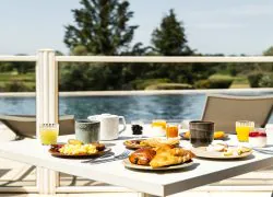 Table blanche sur la terrasse du restaurant séminaire, face à la piscine et au golf, avec viennoiseries, omelette, bacon, crêpes et autres délices du matin.