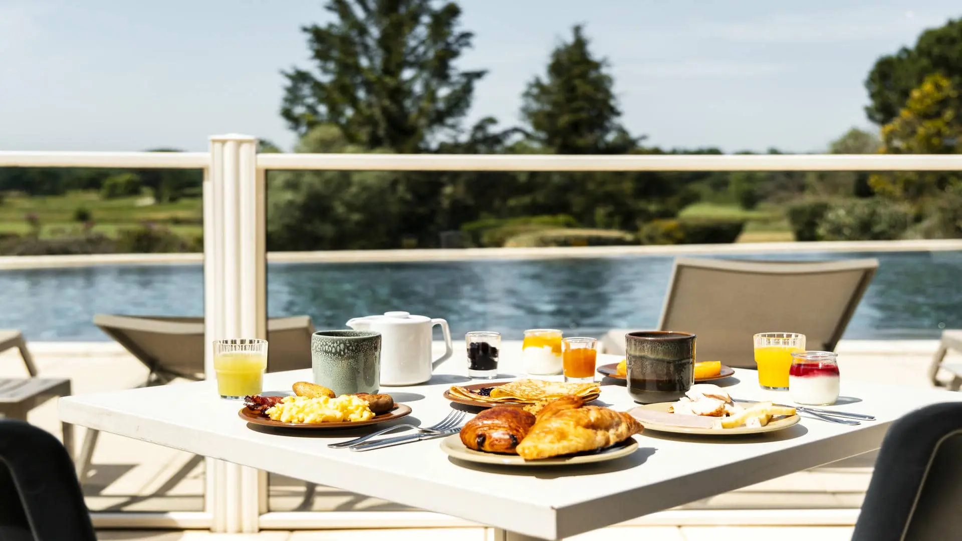Table blanche sur la terrasse du restaurant séminaire, face à la piscine et au golf, avec viennoiseries, omelette, bacon, crêpes et autres délices du matin.