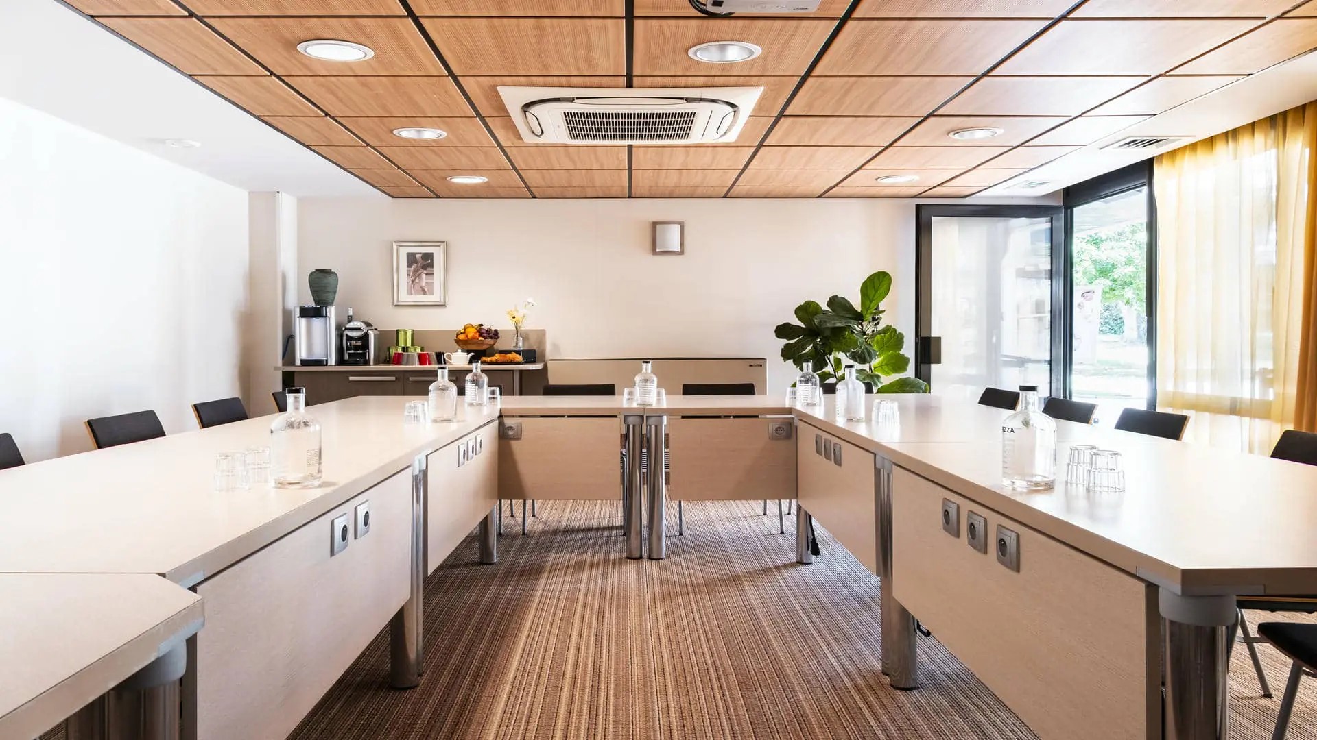 Salle de réunion avec tables en bois disposées en U, moquette beige et plafond en bois, voilages orangés et porte ouverte sur le golf environnant.