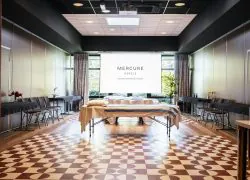 Salle de réunion avec sol en parquet et carrelage rouge et blanc, murs bordeaux, deux tables de massage disposées au centre et rangées de chaises de chaque côté de la salle.