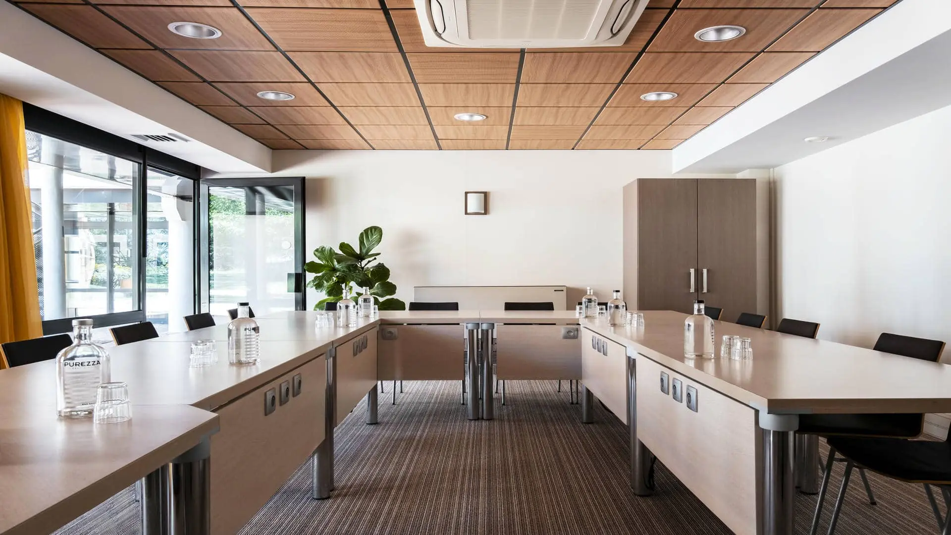 Salle de séminaire avec tables disposées en U et porte ouverte sur l’espace pause extérieur.