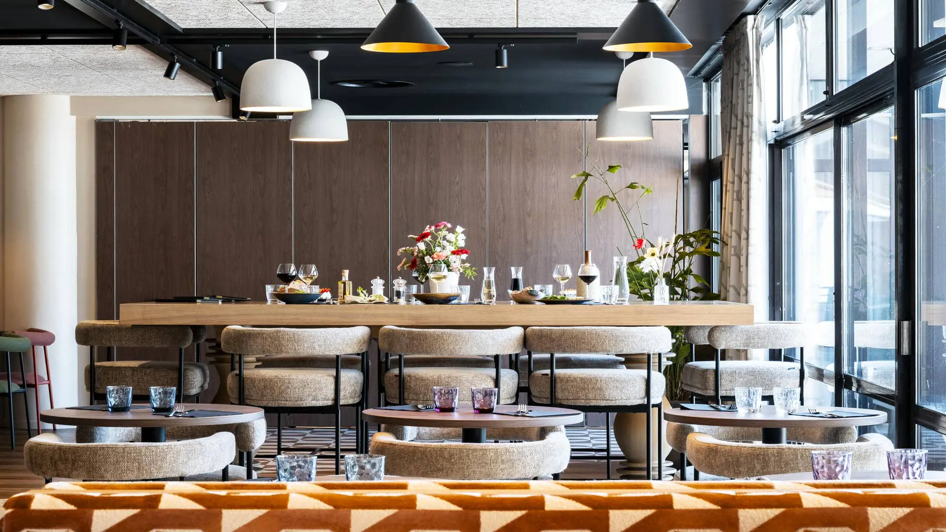Seminar restaurant with a communal table, individual tables for two, fabric chairs and sofa seating, facing the swimming pool and golf course.