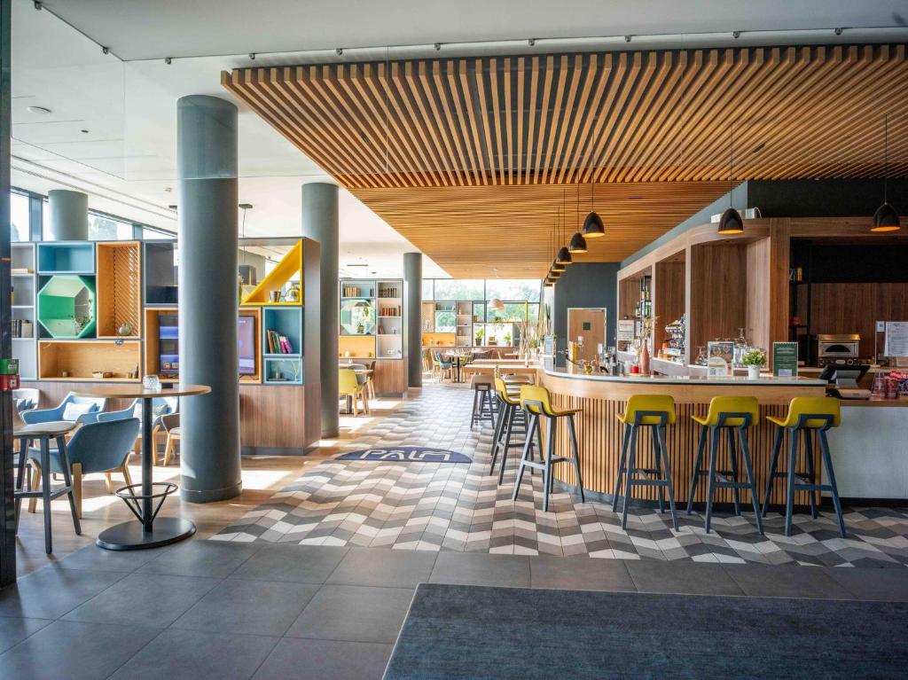 On the right, the seminar bar features a counter and ceiling clad in light wood, with tall yellow chairs. On the left, the restaurant area is divided by colourful shelving units, creating more intimate spaces.