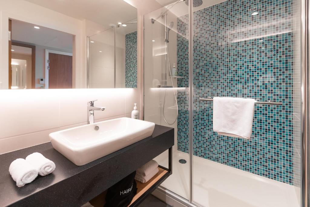 Shower room with blue-toned wall tiles, glass doors, a white washbasin set on a brown vanity unit, and a large wall-mounted mirror.