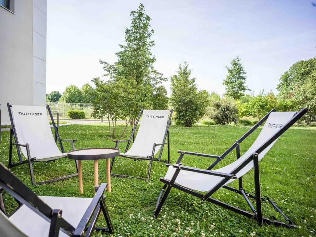 Sun loungers are arranged on the green lawn of the garden, in front of the U-shaped seminar hotel near the airport.