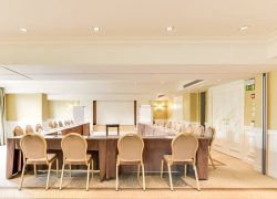 Salle avec table de réunion en U, moquette claire au sol, murs blanc et vert, plafond blanc et écran de projection.