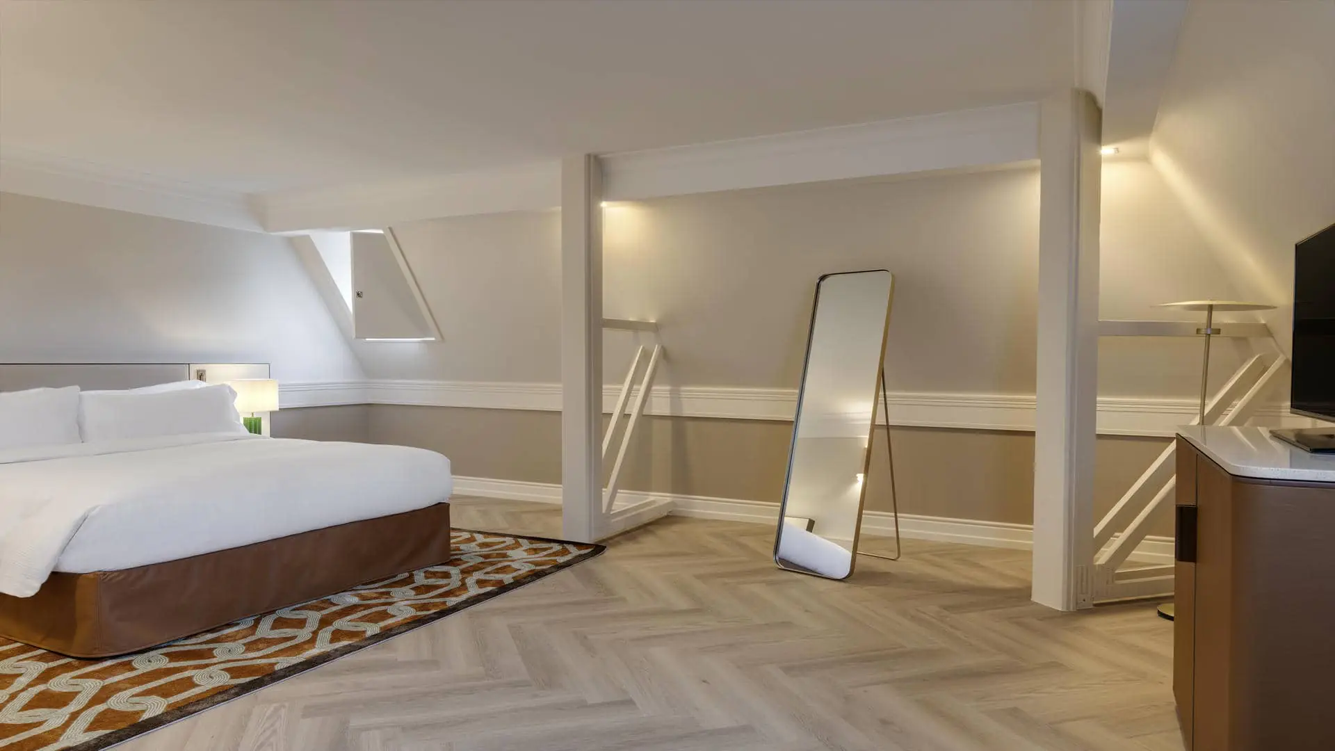 Room with white walls, exposed white beams, a rounded orange-and-brown TV unit, and a gold freestanding mirror.