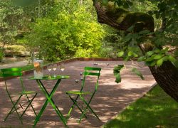 Boulodrome sous les sapins, avec table et chaises vertes en métal, et rosé servi dans trois verres à vin.