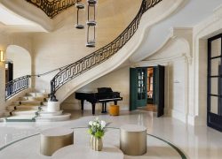 Hall d’entrée en marbre de l’hôtel séminaire, avec escalier revêtu d’un chemin de tissu au centre des marches, piano, et portes noires à carreaux miroirs sur la droite.