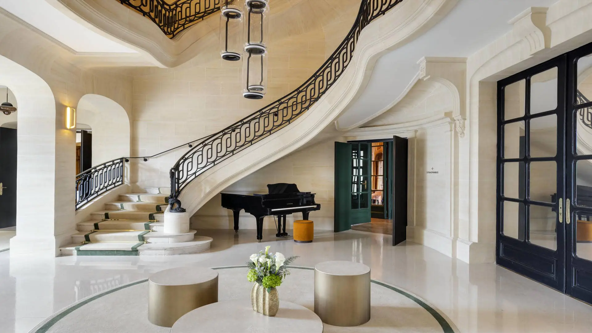 Marble entrance hall of the seminar hotel, with a staircase featuring a fabric runner down the centre of the steps, a piano, and black doors with mirrored glass panels on the right.