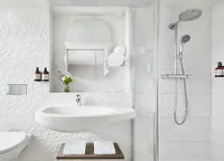 Salle de douche blanche avec carrelage mural texturé, miroir en forme de feuille, lavabo design et étagère en bois.