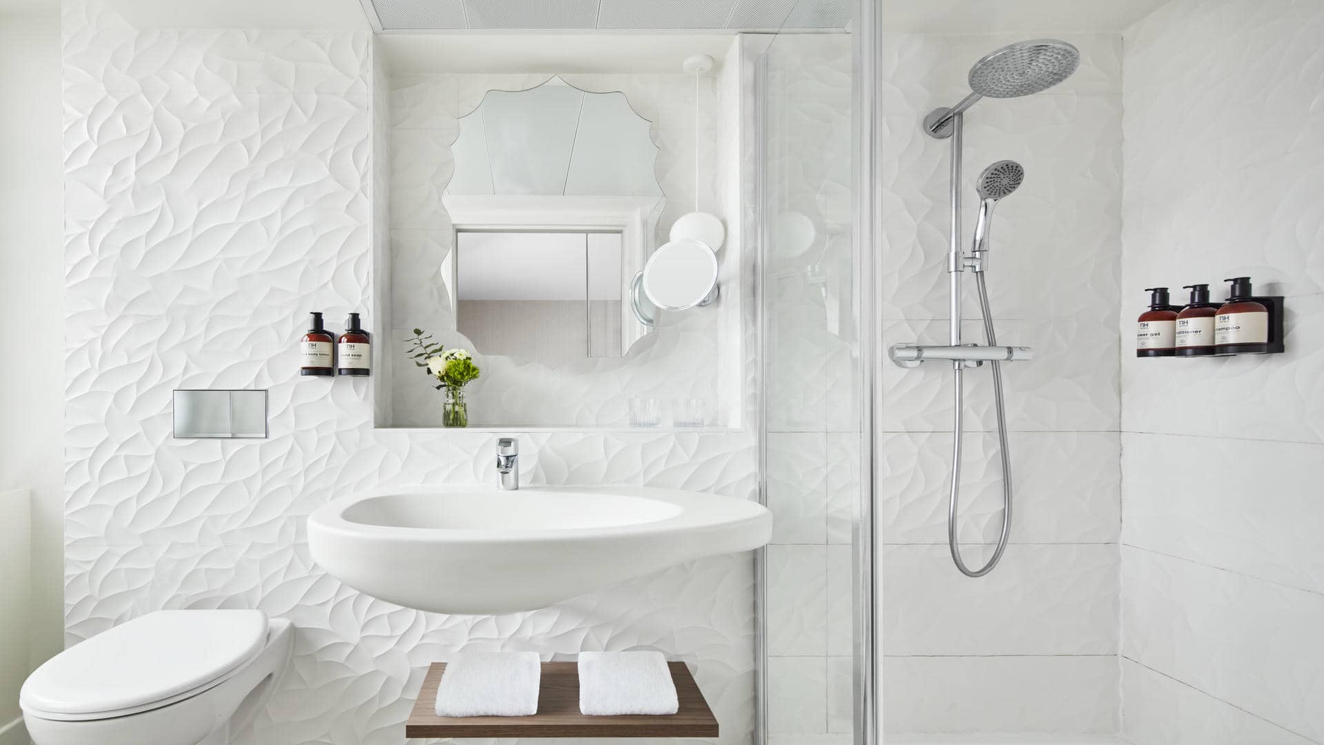Salle de douche blanche avec carrelage mural texturé, miroir en forme de feuille, lavabo design et étagère en bois.