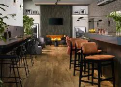 Comptoir de bar avec chaises hautes en tissu terracotta à droite de la salle, tablettes en bois contre le mur en face avec chaises hautes noires pour coworker, cheminée, photographies en noir et blanc et espaces salons.