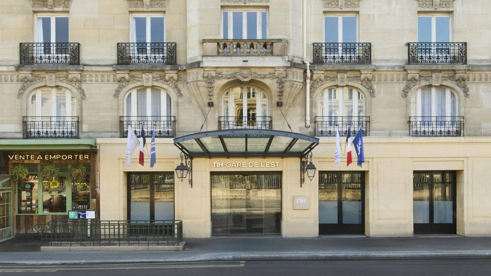 façade haussmanienne avec en rez de chaussée l'entrée du NH Gare de l'est, encadrée de drapeaux, à sa gauche entrée d'un restaurant avec en enseigne vente à emporter