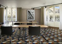 Salle de réunion avec quatre tables en bois, chaises noires, moquette à motifs cylindriques, mur tendu beige, photo en noir et blanc de la Gare de l’Est et grandes fenêtres donnant sur la gare.