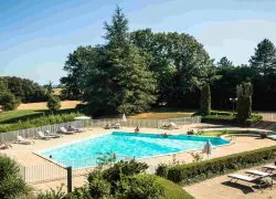 Piscine extérieure avec des personnes installées sur des transats ou dans l’eau, entourée d’un parc arboré.