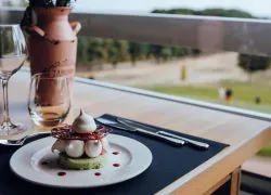 Dessert dressé dans une assiette sur une table en bois, devant une grande baie vitrée donnant sur la campagne, accompagné d’un vase de fleurs en terre cuite, dans un hôtel séminaire au vert.