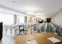 Salle de formation avec un écran de projection, un tableau blanc et un paper board au fond, des chaises grises disposées devant, ainsi qu’un pupitre placé à l’avant de la salle.