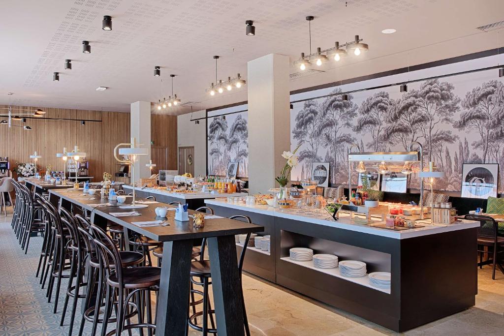 en:: seminar hotel restaurant with a black-and-white forest mural, dark wood buffet counter, and dark wooden tables and chairs in the foreground fr:: restaurant d’un hôtel séminaire avec fresque murale de forêt en noir et blanc, meuble buffet en bois foncé et tables et chaises en bois foncé au premier plan
