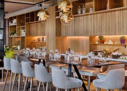 en:: a seminar hotel restaurant with wooden wall shelves, square tables, gray chairs, and gold pendant lights fr:: salle de restaurant d’un hôtel séminaire avec étagères murales en bois, tables carrées, chaises grises et luminaires suspendus dorés