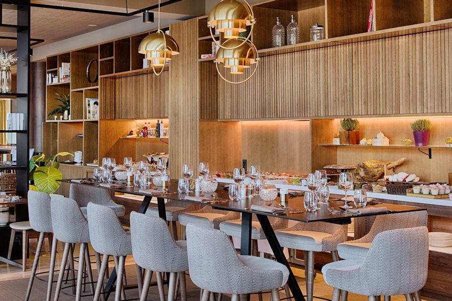 en:: a seminar hotel restaurant with wooden wall shelves, square tables, gray chairs, and gold pendant lights fr:: salle de restaurant d’un hôtel séminaire avec étagères murales en bois, tables carrées, chaises grises et luminaires suspendus dorés