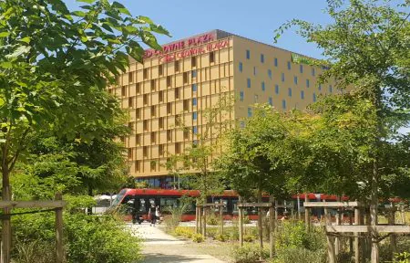 The imposing yellow facades of the Crowne Plaza Nice and the Holiday Inn Express. A tram passes in front of the hotels, surrounded by greenery and parks.