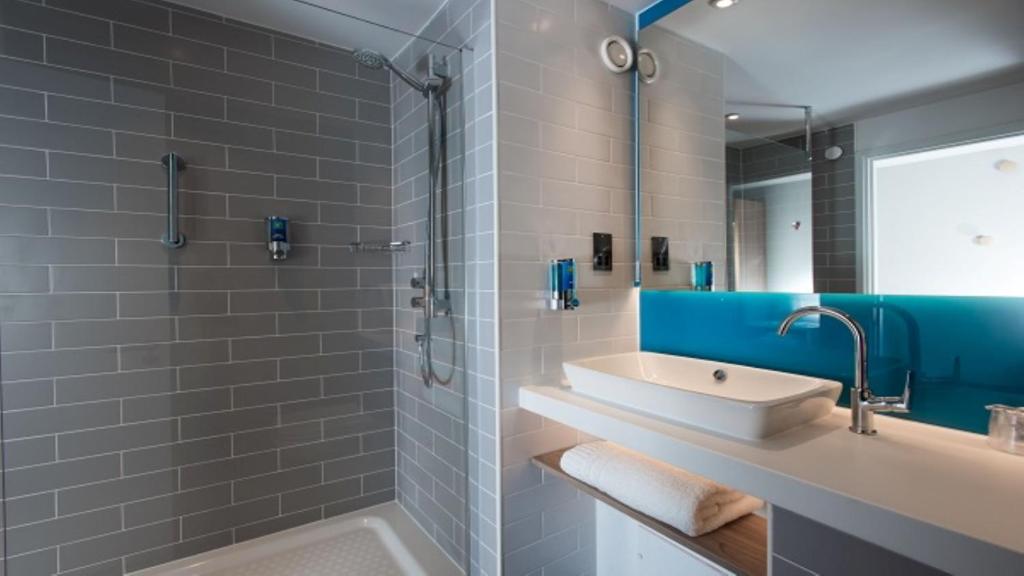 Hotel seminar room shower with a grey tiled wall, a large blue-framed mirror, and a white washbasin