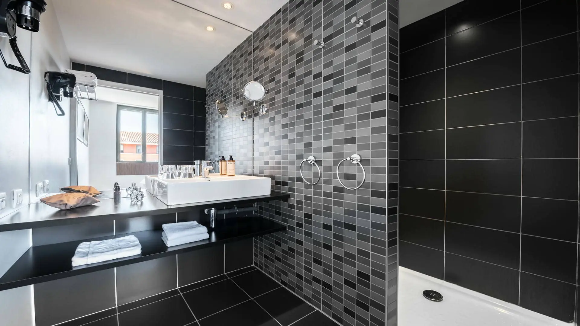 A bathroom with black and grey tiling, a white washbasin, and a walk-in shower.