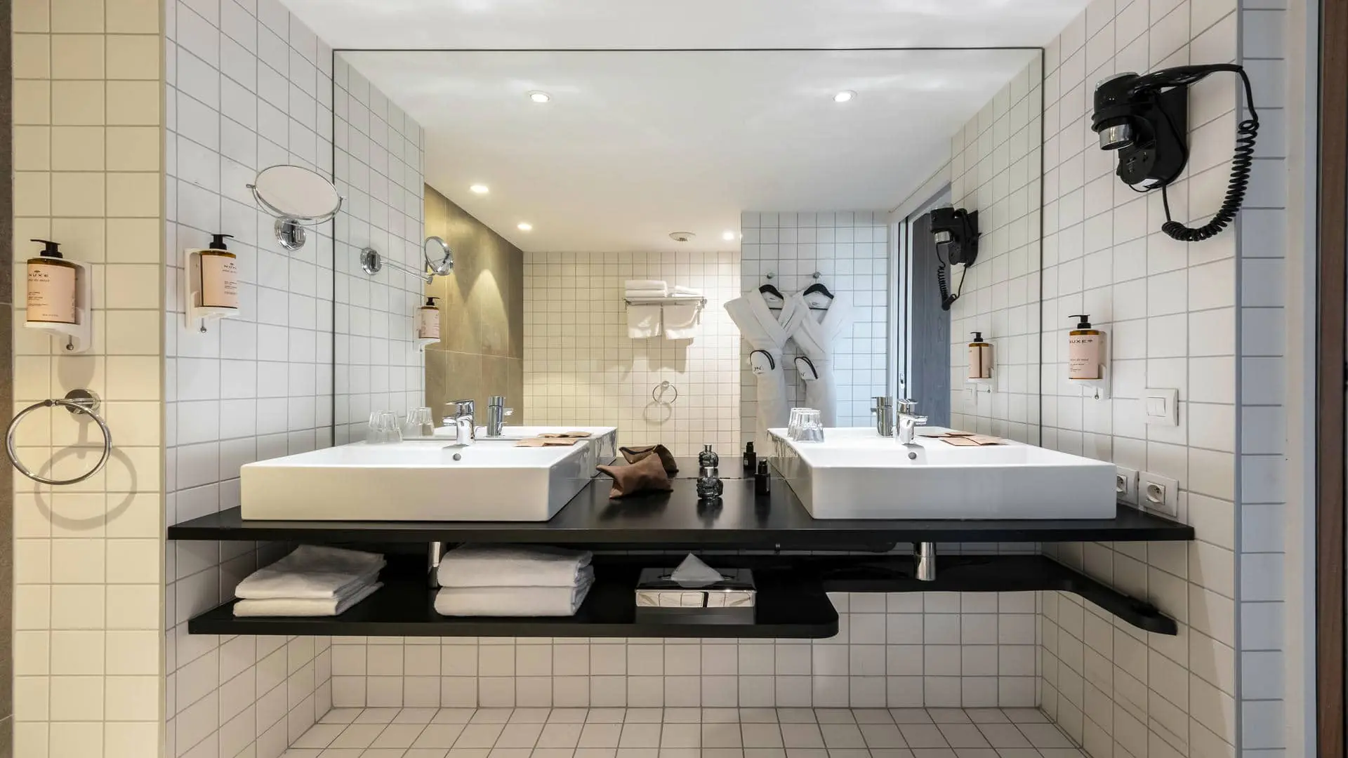 Bathroom equipped with a white double square washbasin, a large mirror, and bathrobes hanging on hangers.