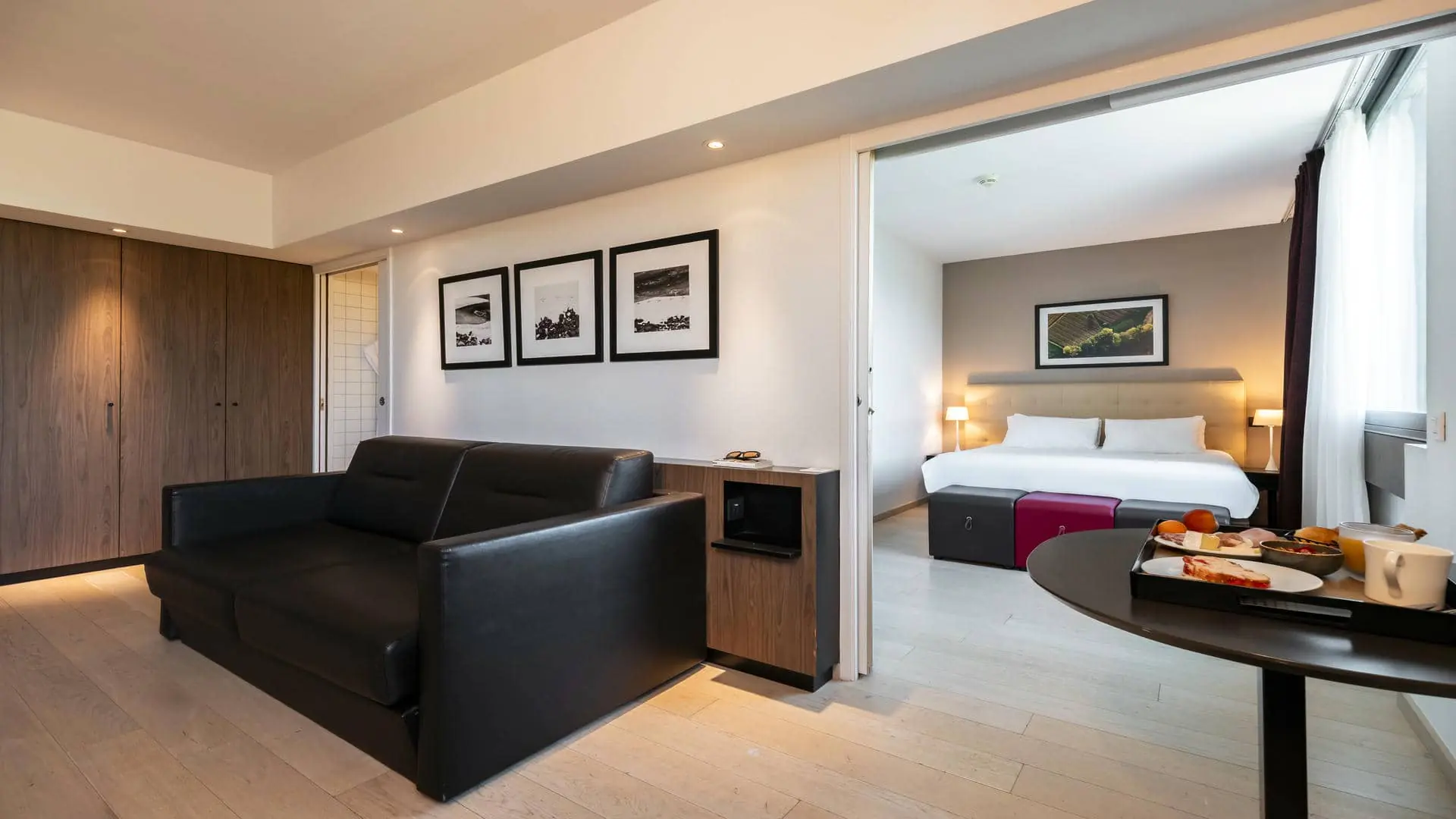 A hotel suite with a leather lounge area and parquet flooring, separated from the bedroom, which features a headboard.