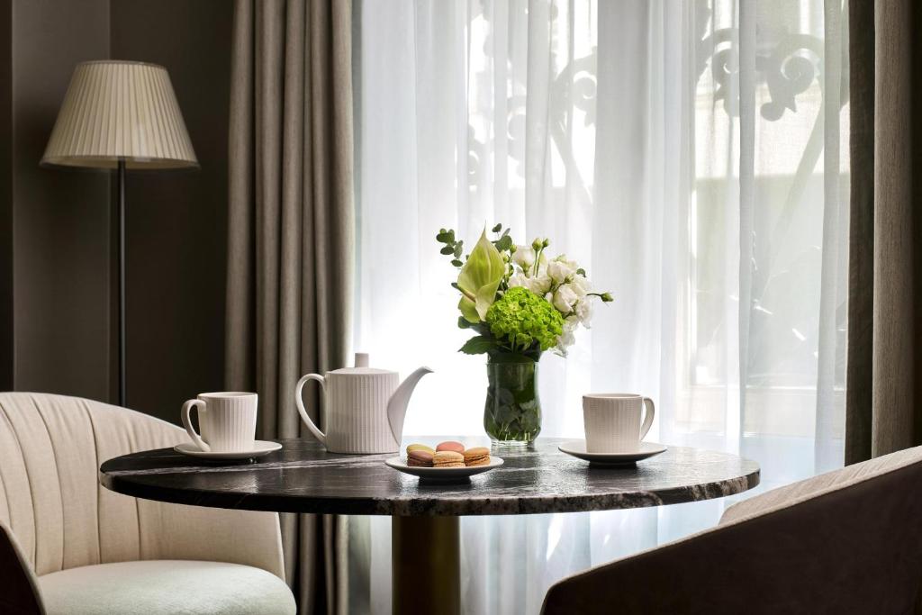 Elegant lounge area bathed in natural light, featuring a round marble table set for two, fine porcelain tea service, delicate pastries and a refined floral arrangement. An intimate, welcoming atmosphere evoking the comfort and sophistication of a luxury hotel.