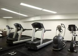 Modern fitness room with treadmills and elliptical machines on a black floor. Large wall mirror, white walls and ceiling spotlights. Dumbbells are placed on the floor.